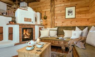A cozy living space with wood paneling and an open fireplace. Tea cups are on the table and a blanket is draped over the couch.