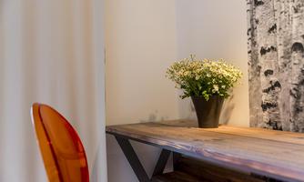 A wooden desk stands against the wall, decorated with a pot full of flowers. In the background, there is a picture of birch trees.