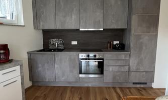 A modern kitchen with gray cabinets and a stove. The floor is made of light wood and there is a window with natural light.