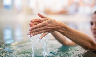 A hand dives into the water and splashes water. In the background, a blurred area is visible.