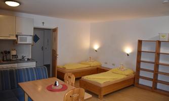 A cozy room with two beds and a dining table. The kitchenette is well equipped and there is plenty of daylight.