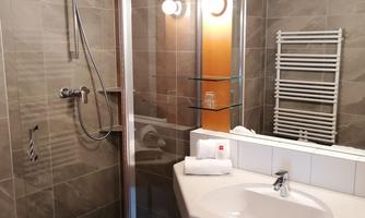 A modern bathroom with a shower and a sink. The walls are painted in neutral gray tones and there are towels on the washbasin.