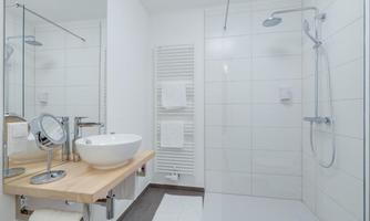A modern bathroom with a shower and a sink. The walls are light tiled and there are fresh towels.