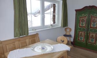 A cozy room with a wooden table and chairs. Next to the window stands a beautiful, brightly painted wardrobe.