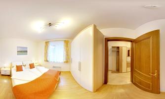 A bright bedroom with two beds and orange blankets. In the background, a door and a bathroom are visible.