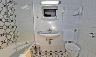 A modern bathroom with a shower, sink, and toilet. The walls are tiled, and there is a stylish black-and-white pattern on the floor.
