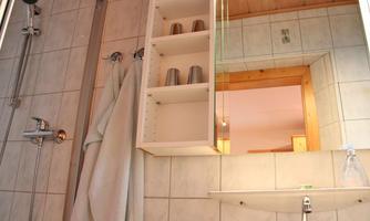A modern bathroom with a shower and a large mirror. In the background, towels and glasses are visible on a shelf.
