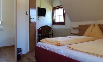 A cozy room with a double bed and wooden floor. The room has a television and a chair.