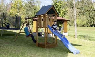 An outdoor playground with a slide and a swing. Two children are having fun playing in the grass.