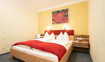 A cozy bedroom with a double bed and red pillows. A colorful painting hangs on the wall, and there are nightstands as well as a pleasant wall color.