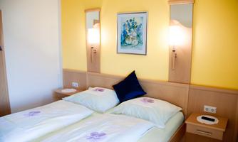 A comfortable hotel room with two beds and a bright, friendly wall color. A picture hangs on the wall and there are modern bedside lamps.