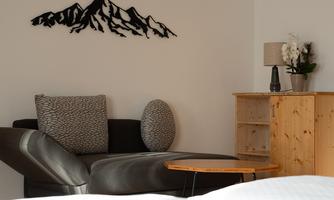 A cozy room with a modern sofa and a wooden dresser. On the wall, there is a decorative mountain silhouette.