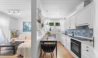 A modern kitchen unit with white cabinets and a bright, friendly atmosphere. In the foreground is a dining table with a chair that creates a cozy living ambiance.