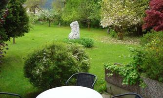 A beautiful garden with green grass and various plants. In the middle stands an artistic statue.