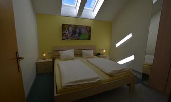 A cozy bedroom with a double bed and a colorful mural. Large windows let in plenty of daylight.