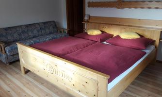 A cozy bedroom with a large wooden bed and red bedding. Next to the bed is a blue couch in a bright room.