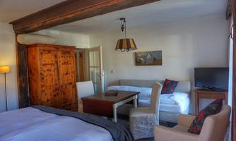 A cozy room with a double bed, a table and seating. There is a wardrobe and a TV.