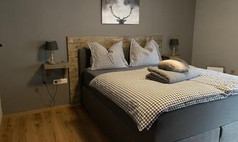 A modern bedroom with a large double bed and checked bedding. Two bedside lamps hang on the walls and there is a decorative picture of a deer.