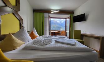 A cozy room with a large bed, colorful pillows, and a view of the mountains. A window opens the space to nature and provides plenty of daylight.