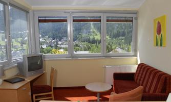 A bright room with a cozy sofa and a table.  
Large windows offer a view of the mountains and the landscape.