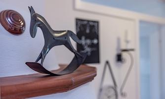 A decorative horse sculpture made of metal stands on a shelf. In the background, additional wall decorations can be seen.