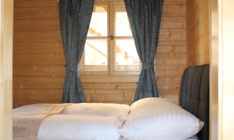 A cozy bedroom with wooden paneling and a large bed. The windows are decorated with blue curtains.