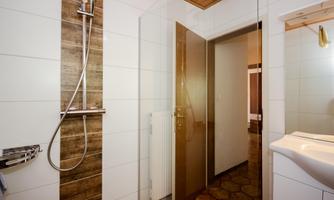 A modern bathroom with a shower and bright tiles. In the background, a mirror and an entrance to another room are visible.