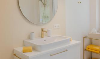 A modern bathroom with a white sink and a round mirror. Yellow towels and an elegant shower cubicle complement the appealing design.
