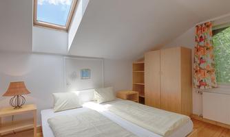 A bright bedroom with two single beds and a window with a skylight. There is a dresser and a nightstand with a lamp.