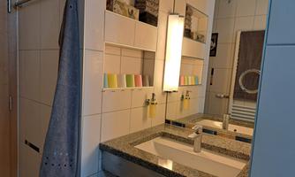 A modern bathroom with a sink and a large mirror. Towels hang on the wall, and colored cards are arranged on a shelf.