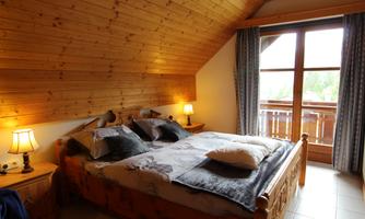 A cozy bedroom with a wooden bed and a large window. The walls are paneled with wood and there is soft lighting from table lamps.