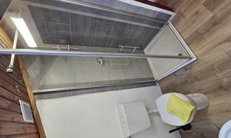 A modern bathroom with a shower cabin and a toilet. The floor is made of wood and the walls are tiled.