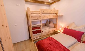 A cozy bedroom with a loft bed made of light wood and a single sleeping option. The bedding is in warm shades of red, and a small lamp creates an inviting atmosphere.