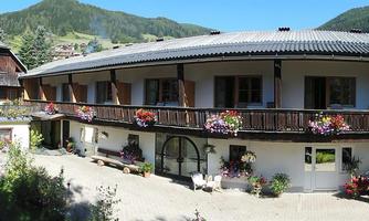 A charming building in alpine style with a balcony full of flowers. Surrounded by green mountains and a peaceful atmosphere.