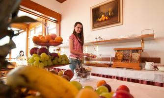 A breakfast room with a rich fruit buffet. A young woman stands at the table and serves herself fresh fruit.