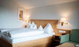 A cozy bedroom with a wooden bed and white bedcovers. Next to the bed is a green couch and there is soft lighting.
