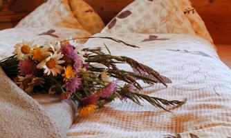 A cozy bed with loft beds and birch-colored wood. Next to it lies a colorful bouquet on the bedspread.
