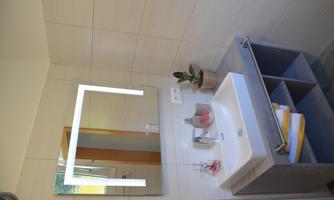 A modern bathroom with a sink and a large mirror. The walls are bright tiled, and a small plant sits on the sink.