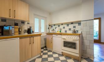 A modern kitchen with wooden cabinets and a gas stove. The floor is tiled with blue and white tiles.