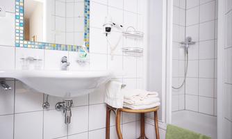 A bright bathroom with white tiles and a sink. Towels and a shower are clearly visible.