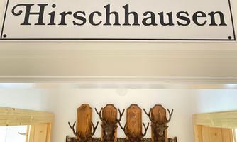 A sign with the inscription "Hirschhausen" hangs on the wall. Below it are several wooden antler trophies displayed.