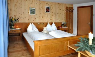 A cozy bedroom with a large double bed and wooden furniture. The walls are made of wood, and there is a small decoration on the table.