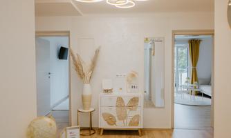 A modern entrance with light wooden flooring and stylish decorative elements. The wall is decorated with a large mirror and plant motifs.