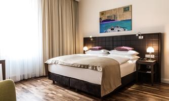 A modern hotel room with a large double bed and soft colors.  
Soft curtains let light in and create an inviting atmosphere.