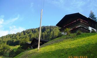 A charming area with green meadows and wooded hills. In the foreground, two alpine houses stand, surrounded by a picturesque landscape.