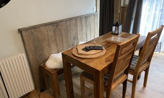 A rustic dining area with a wooden table and two chairs. On the table is a round placemat and some items.