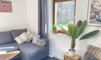 A cozy living area with a gray sofa and a wooden table. The window lets in a lot of light, and a plant is on a table next to the window.