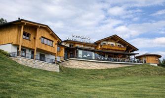 A modern restaurant in alpine style with wood paneling. It is situated on a gentle hill and offers a terrace with views of the surrounding area.