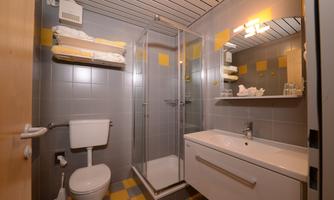 A modern bathroom with a shower, sink, and wall mirror. The walls are designed with gray and yellow tiles.