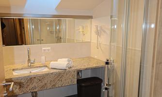 A modern bathroom with a shower and a large sink. The walls are light, and there is a natural light source from a skylight.